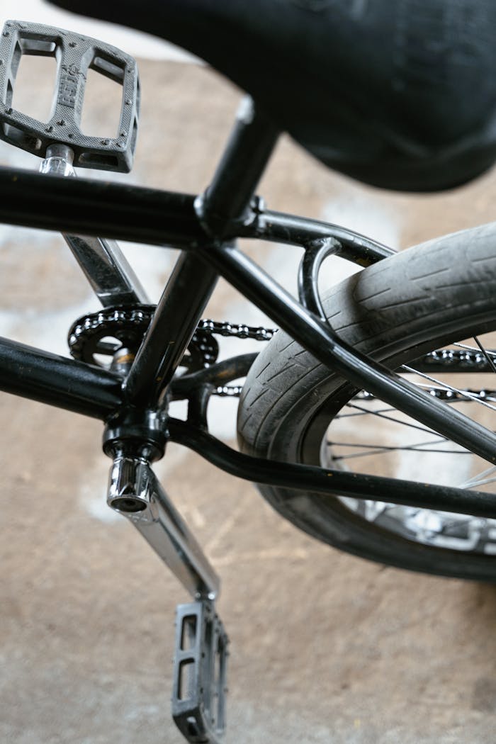 Detailed view of a black bicycle frame, pedals, and tire showcasing sleek design.